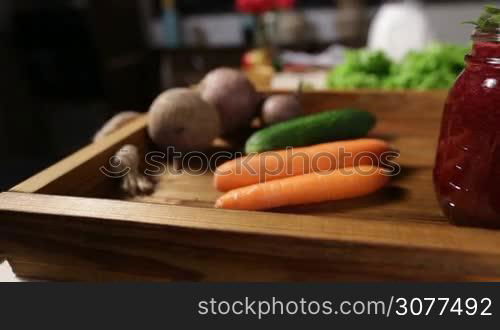 Mason jar of fresh detox beetroot smothie with vegetable ingredients on wooden tray over rustic kitchen background closeup. Healthy vegetable smoothie in mason jar with straw and mint leaf on tray. Dieting, vegetarian, fitness, healthy lifestyle.