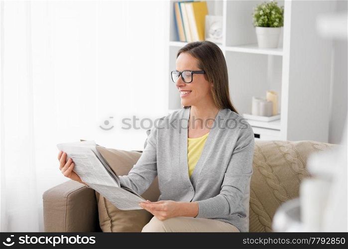 mass media and people concept - happy middle-aged woman reading newspaper at home. happy woman reading newspaper at home