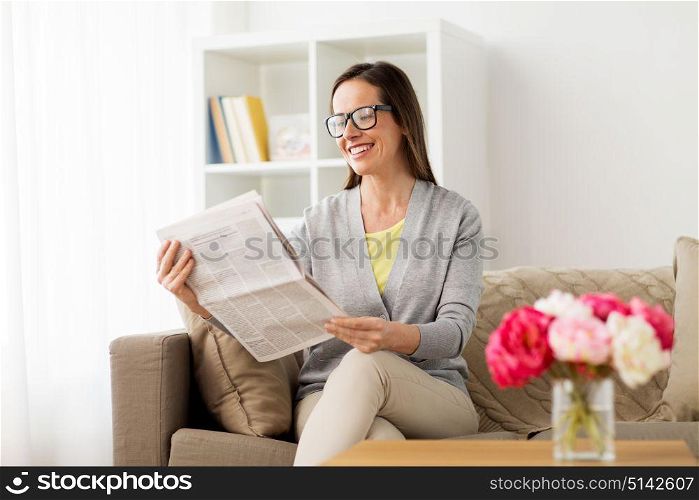 mass media and people concept - happy woman reading newspaper at home. happy woman reading newspaper at home