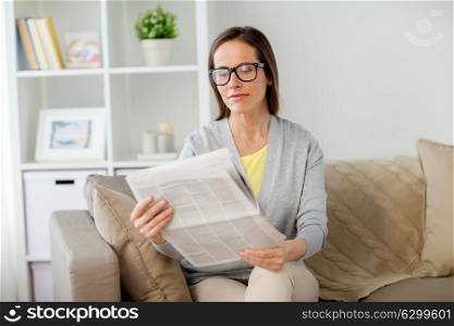 mass media and people concept - woman in glasses reading newspaper at home. woman in glasses reading newspaper at home
