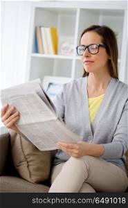 mass media and people concept - woman in glasses reading newspaper at home. woman in glasses reading newspaper at home. woman in glasses reading newspaper at home