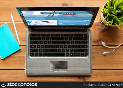 mass media, business and technology concept - close up of laptop computer with world news web page on screen on wooden table