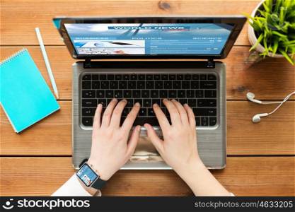 mass media, business, people and technology concept - close up of woman or student typing on laptop computer with world news web page on screen notebook and earphones on wooden table