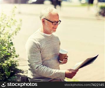 mass media, news and people concept - senior man reading newspaper and drinking coffee in city. senior man reading newspaper and drinking coffee