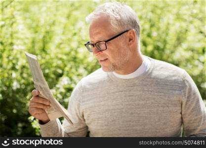 mass media, news and people concept - senior man reading newspaper in city. senior man reading newspaper