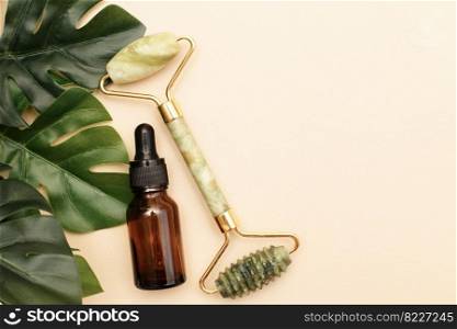 Massage quartz roller for the face of natural nephritis with serum oil in brown glass bottle with monstera leaves on beige background.. Massage quartz roller for the face of natural nephritis with serum oil with monstera leaves on beige background.