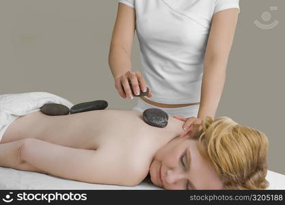 Massage therapist placing pebbles on a mature woman&acute;s back