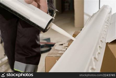 Master applies glue to the baseboard with a glue gun, hands close-up. The process of installing a ceiling plinth.