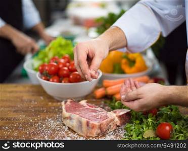 Master Chef hands putting salt on juicy slice of raw steak with vegetables around on a wooden table. Chef putting salt on juicy slice of raw steak