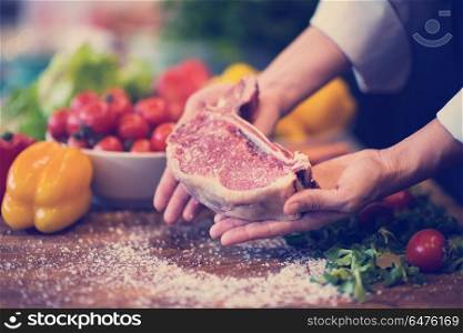 Master Chef holding juicy slice of raw steak with vegetables around on a wooden table. Chef holding juicy slice of raw steak