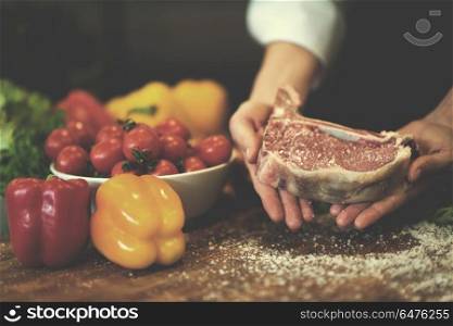 Master Chef holding juicy slice of raw steak with vegetables around on a wooden table. Chef holding juicy slice of raw steak