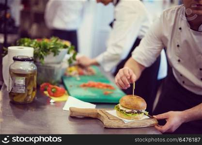 master chef putting toothpick on a burger in restaurant kitchen. chef finishing burger