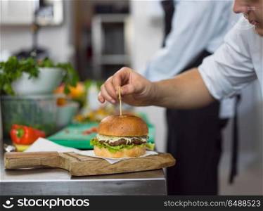 master chef putting toothpick on a burger in restaurant kitchen. chef finishing burger