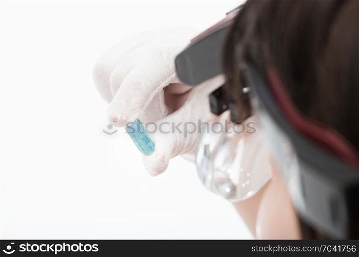 master in head wearing magnifying glasses checks aquamarine crystal on whie background