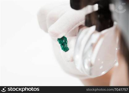master in head wearing magnifying glasses inspects dioptase crystal on whie background