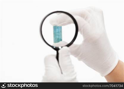 master inspects aquamarine crystal with magnifier on white background
