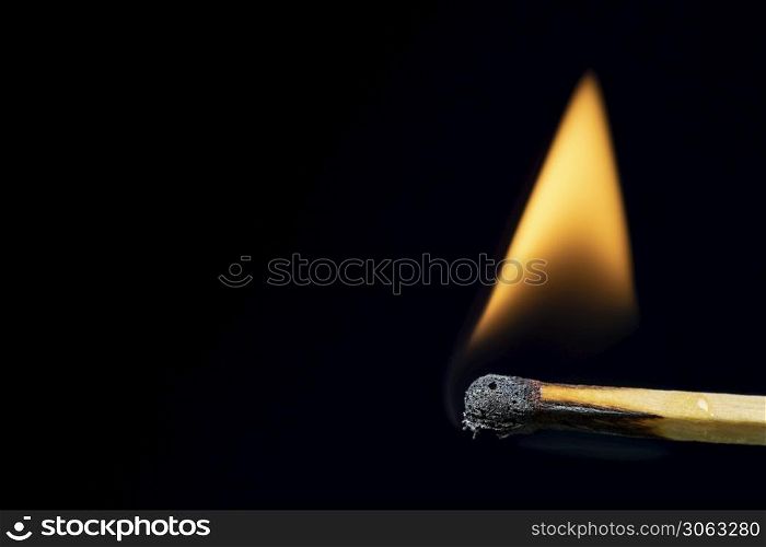 Match burning after being lit showing flame against black background with large copy space.