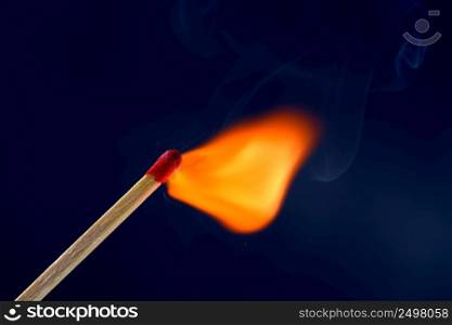 Match stick ignited burning bright big fire flame with blue smoke on dark background.
