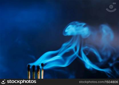 Matches just extinguished in a mystical dark blue light against a dark background. Spectacular smoke. Minimalism, place for text.