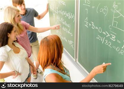 Math lesson student write on green chalkboard with classmates pointing