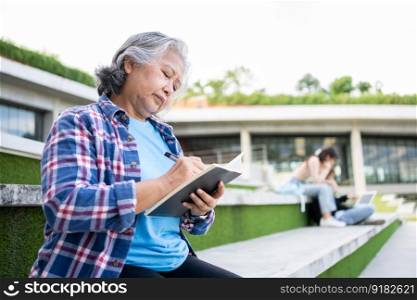 Mature adult student sitting in front off College building and reading school books after attending a university class, Adult education Learning Studying Happy Asian Elderly retired activity