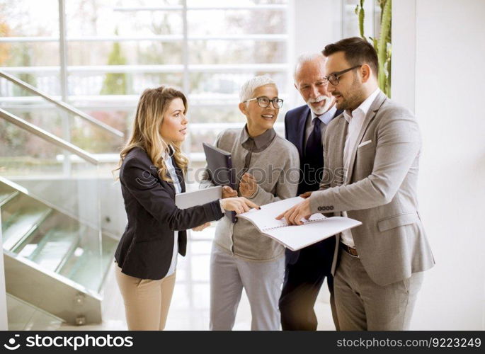 Mature and young businesswoman and a businessman standing in the modern office analyzing plan