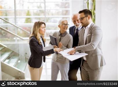 Mature and young businesswoman and a businessman standing in the modern office analyzing plan