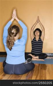 Mature Asian adult female doing yoga with prime adult Caucasian female at gym.