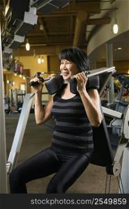 Mature Asian adult female using exercise machine at gym.