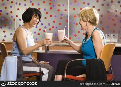 Mature Asian and Caucasian adult females sitting at table in health club cafeteria.