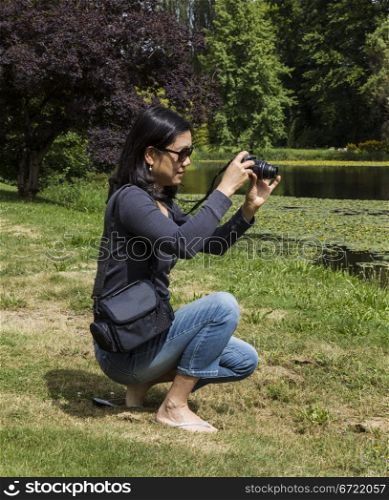 Mature Asian lady taking photos of lake with trees in background