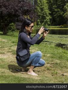 Mature Asian lady taking photos of lake with trees in background