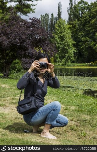Mature Asian lady with small camera with lake, trees and sky in background