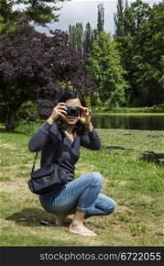 Mature Asian lady with small camera with lake, trees and sky in background