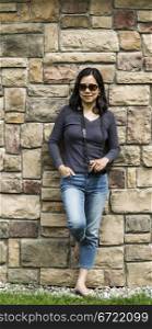 Mature Asian women holding camera with stone wall in background- full body shot