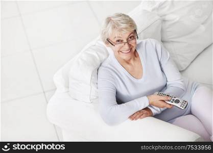 Mature attractive woman with a remote control from a TV on a white sofa