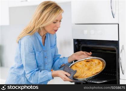 mature blond woman baking tart in oven