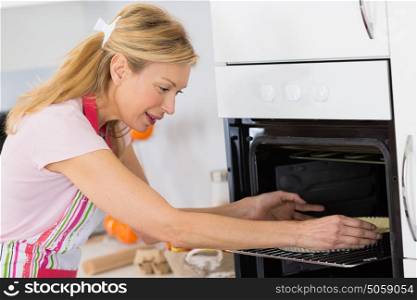 mature blond woman putting tart in oven