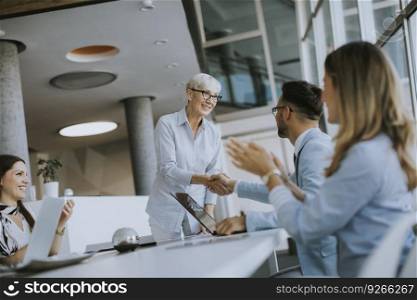 Mature business woman handshaking with young colleague on a meeting in the office