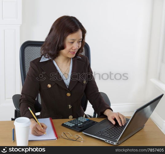 Mature business woman preparing to take notes while looking at the computer monitor. Background is white walls.