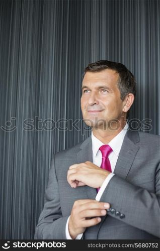 Mature businessman buttoning sleeve against wall