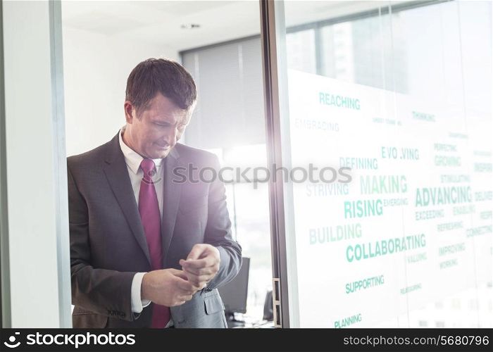 Mature businessman buttoning sleeve in office