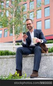 Mature Businessman Checking Mobile Phone Sitting Outside Office