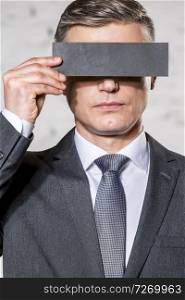 Mature businessman covering eyes with paper against wall at office