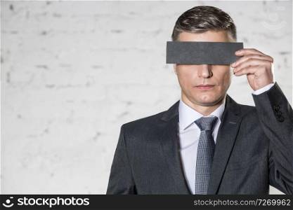 Mature businessman covering eyes with paper against white brick wall at office