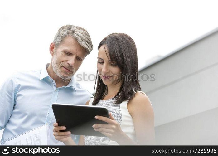 Mature businessman discussing with colleague over digital tablet at terrace in office
