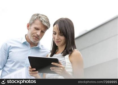 Mature businessman discussing with colleague over digital tablet at terrace in office