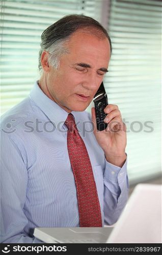 mature businessman looking at his laptop and talking on his cell