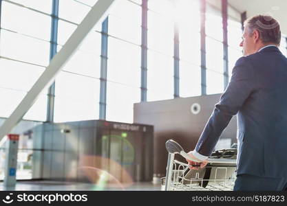 Mature businessman pushing luggage cart for check in at airport