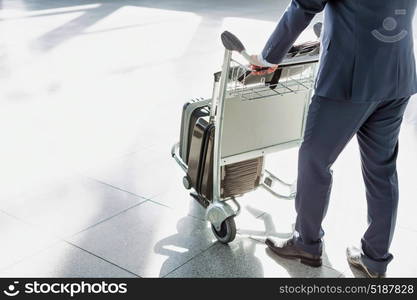 Mature businessman pushing luggage cart for check in at airport